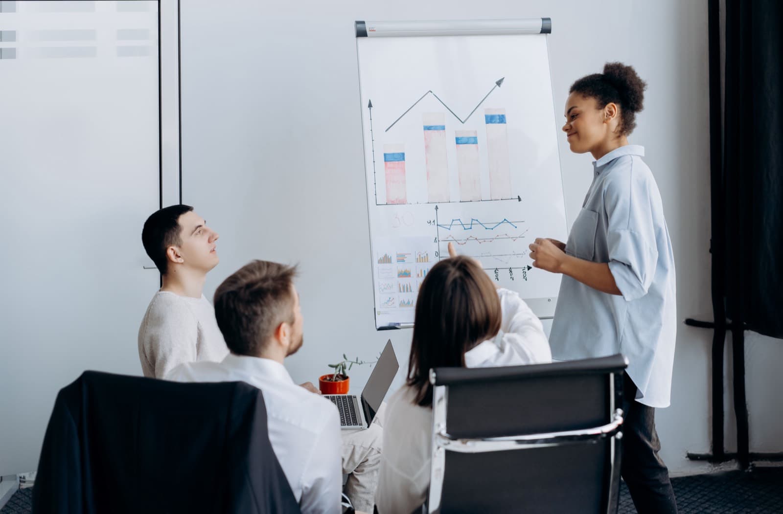 Líder em pé diante de um flipchart com gráficos desenhados à mão, conduzindo a conversa com o time sentado
